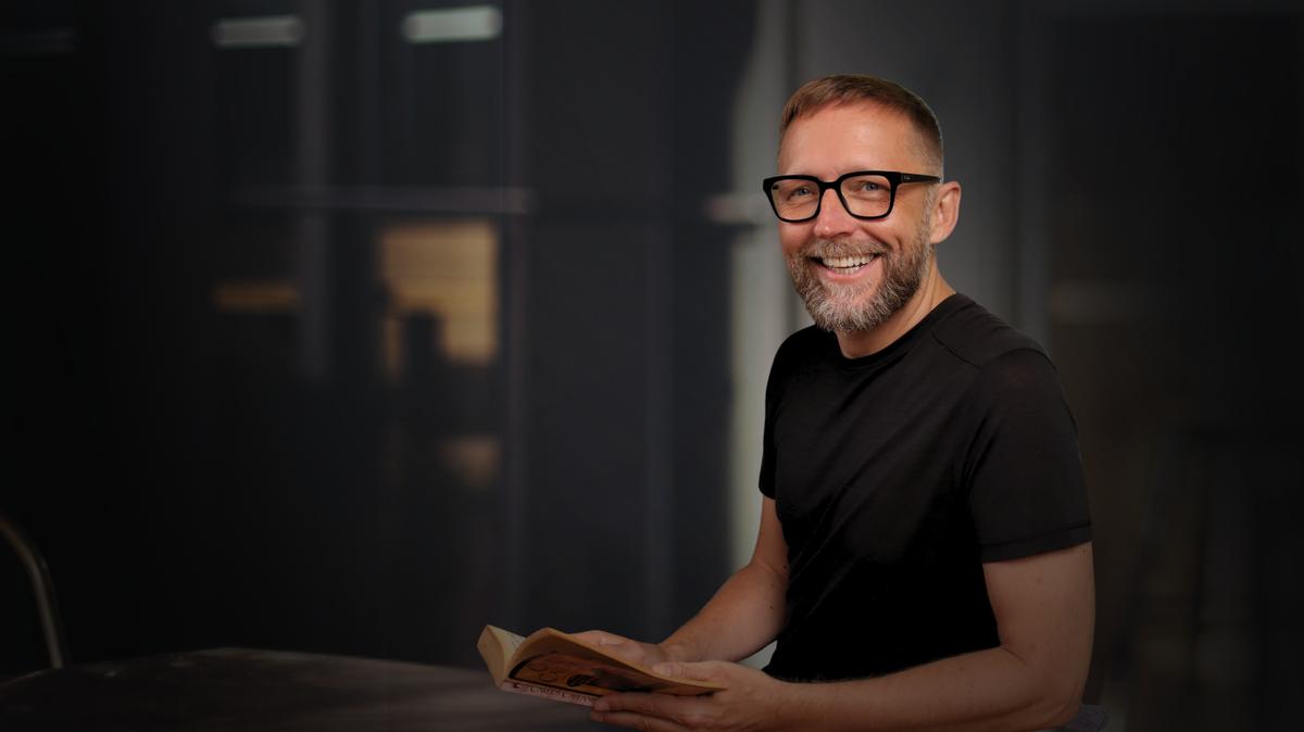 Markus Asano mit einem Buch, Kopf leicht geneigt, nachdenklich und warm