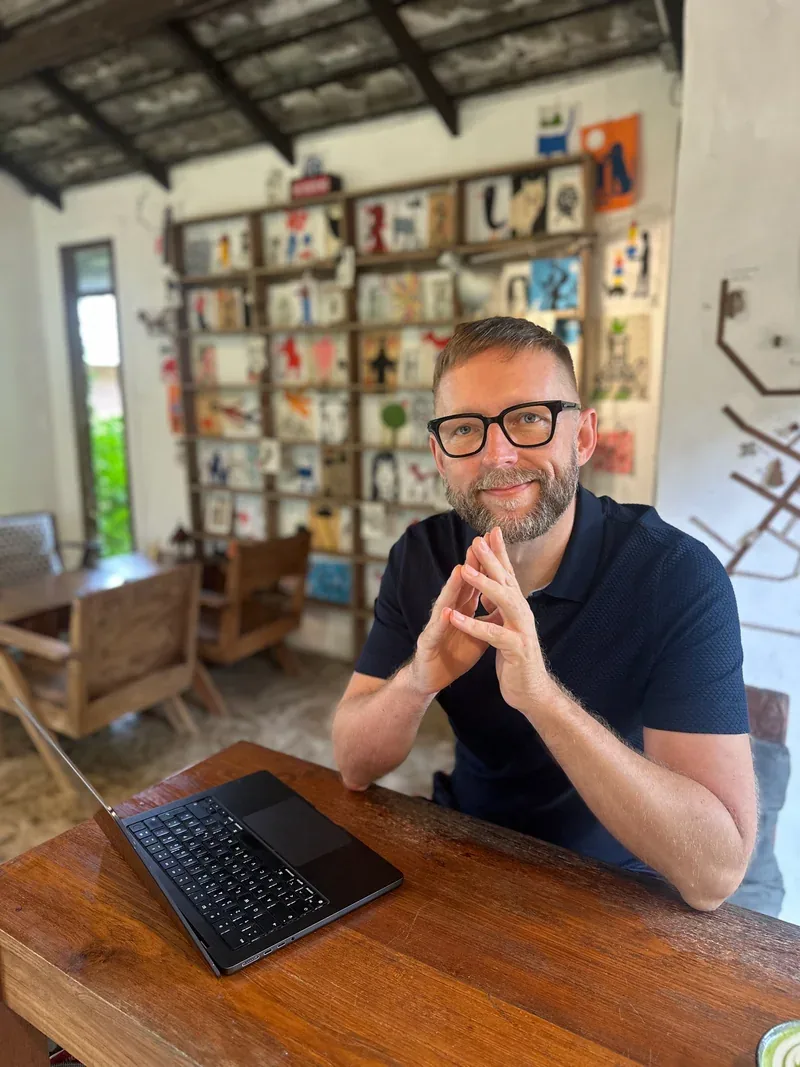 Markus Asano an einem Holztisch mit aufgeklapptem Laptop.