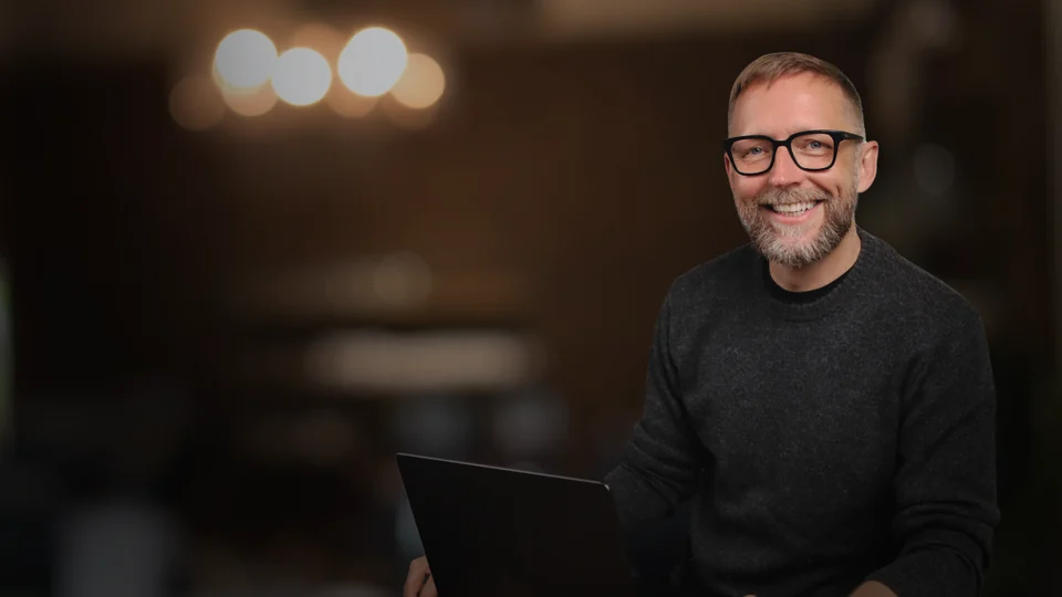 Markus Asano am Laptop vor dunklem Hintergrund.