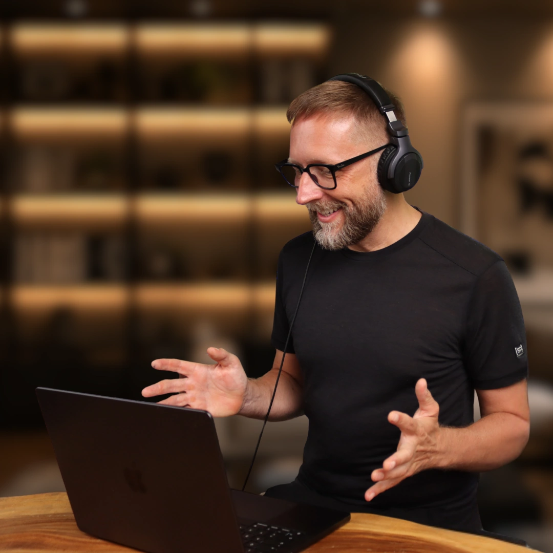 Markus Asano mit Kopfhörern am Laptop, mit beiden Händen erklärend.