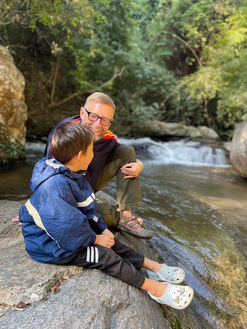 Markus und Milan sitzen gemeinsam am Wasser und lachen miteinander.
